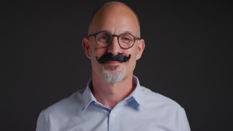 Portrait-Of-Mature-Man-Wearing-Fake-Moustache-Symbolizing-Support-For-Movember-Promoting-Men's-Health-And-Cancer-Awareness